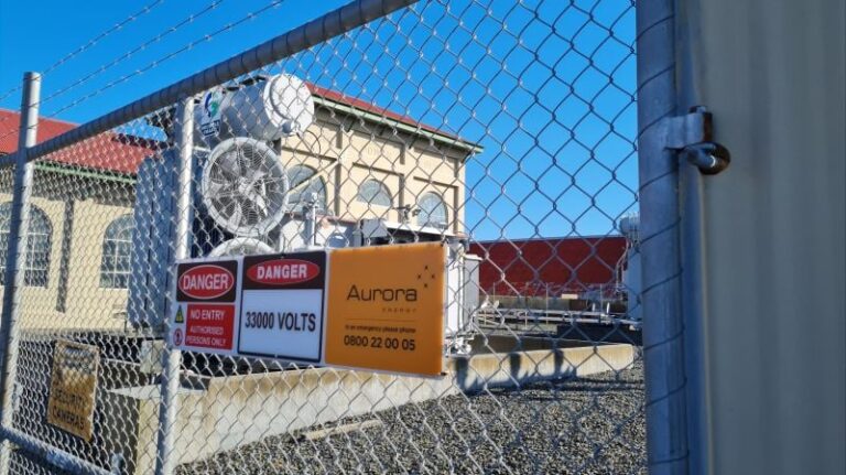 Safety signs on a substation fence warning of 33,000 volts beside an Aurora Energy contact sign