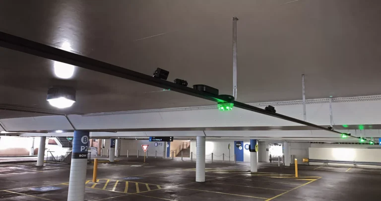 Ceiling-mounted parking sensors with green bay-availability lights above empty bays in a car park